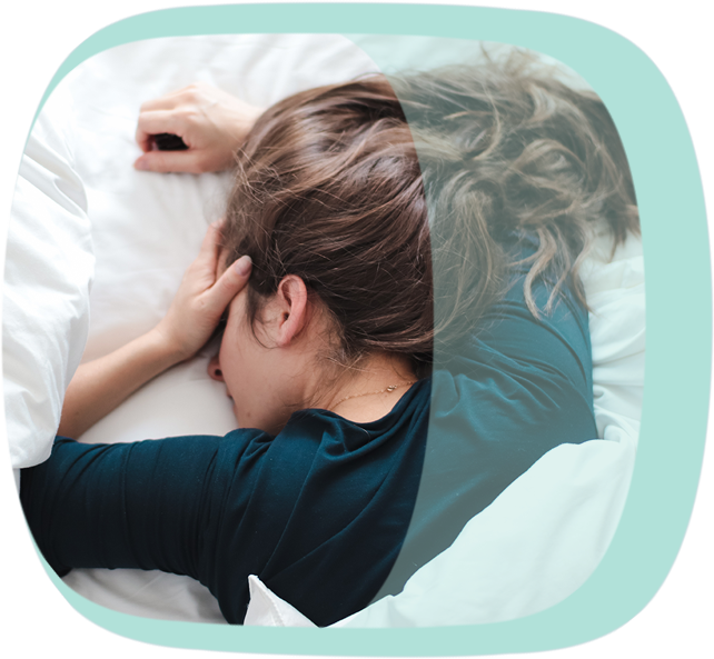 Eine brünette Frau liegt im Bett und hält sich die Augen zu