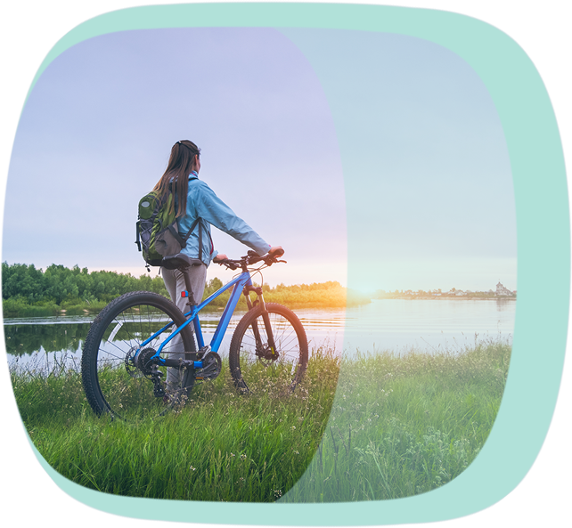 Eine Frau steh mit ihrem Fahrrad am See und betrachtet den Sonnenuntergang